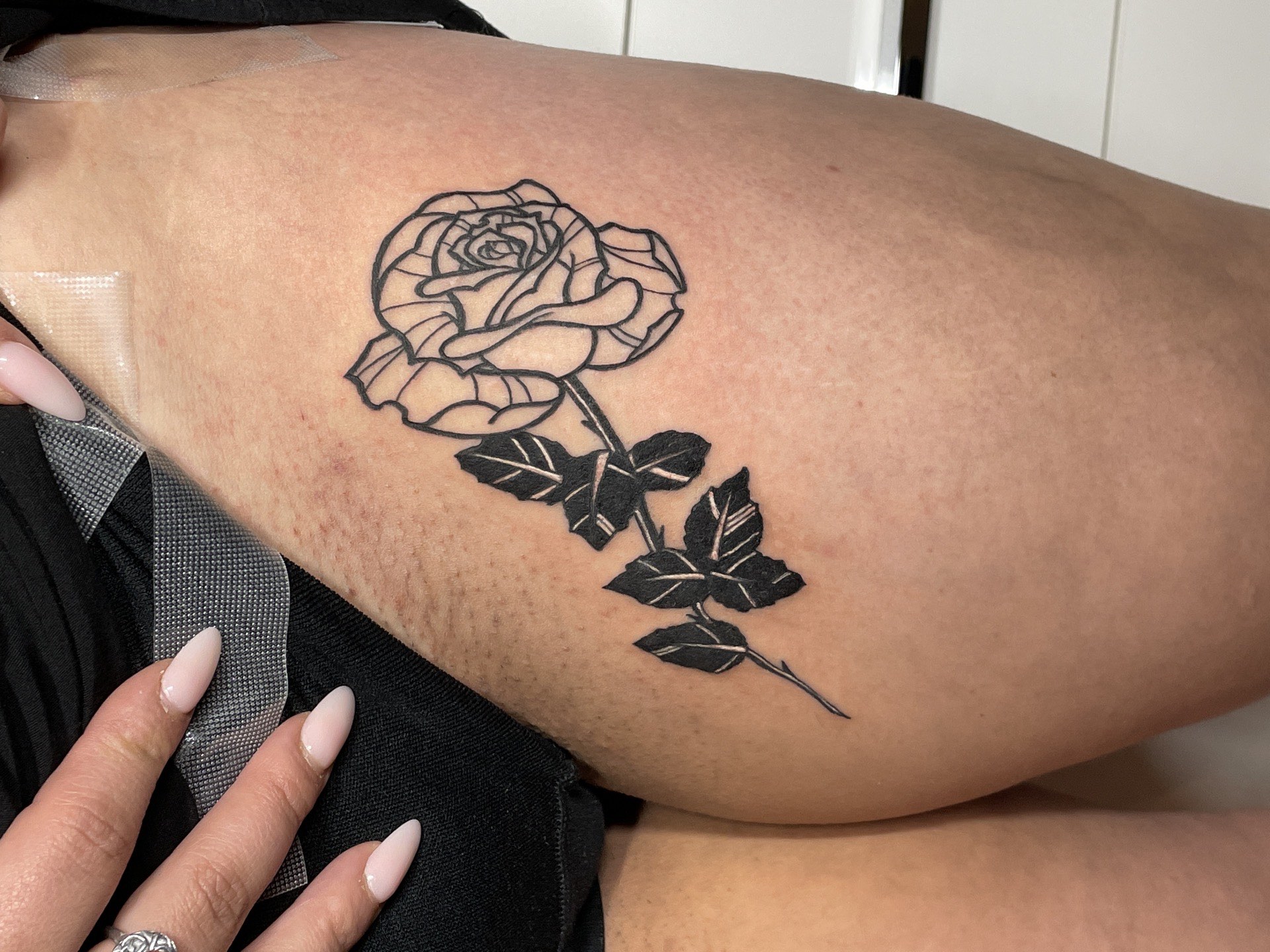 Blackwork tattoo bold rose with stem and leaves on upper arm in Los Angeles