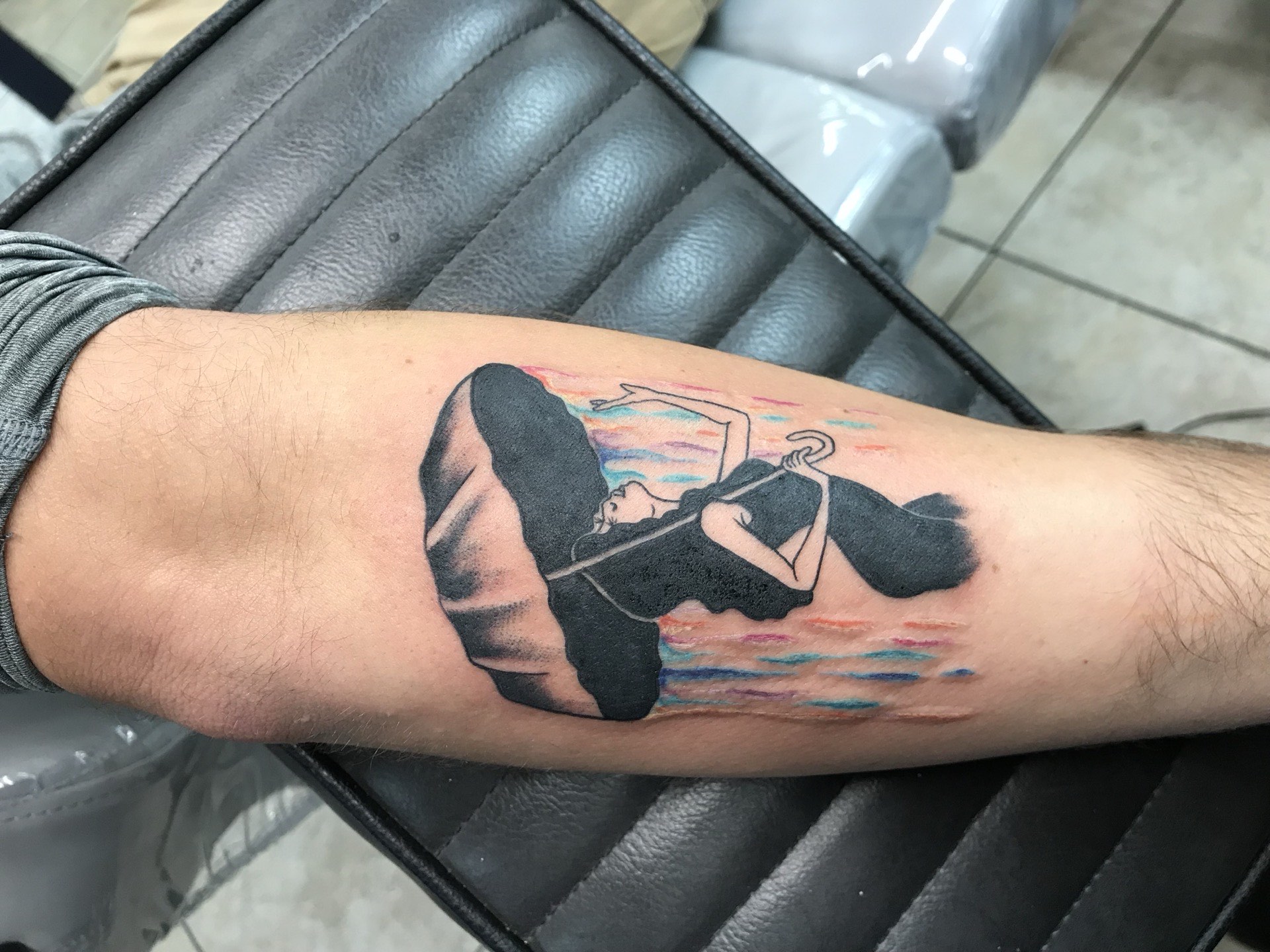 Blackwork tattoo silhouette woman reading with colorful sky on forearm in Los Angeles