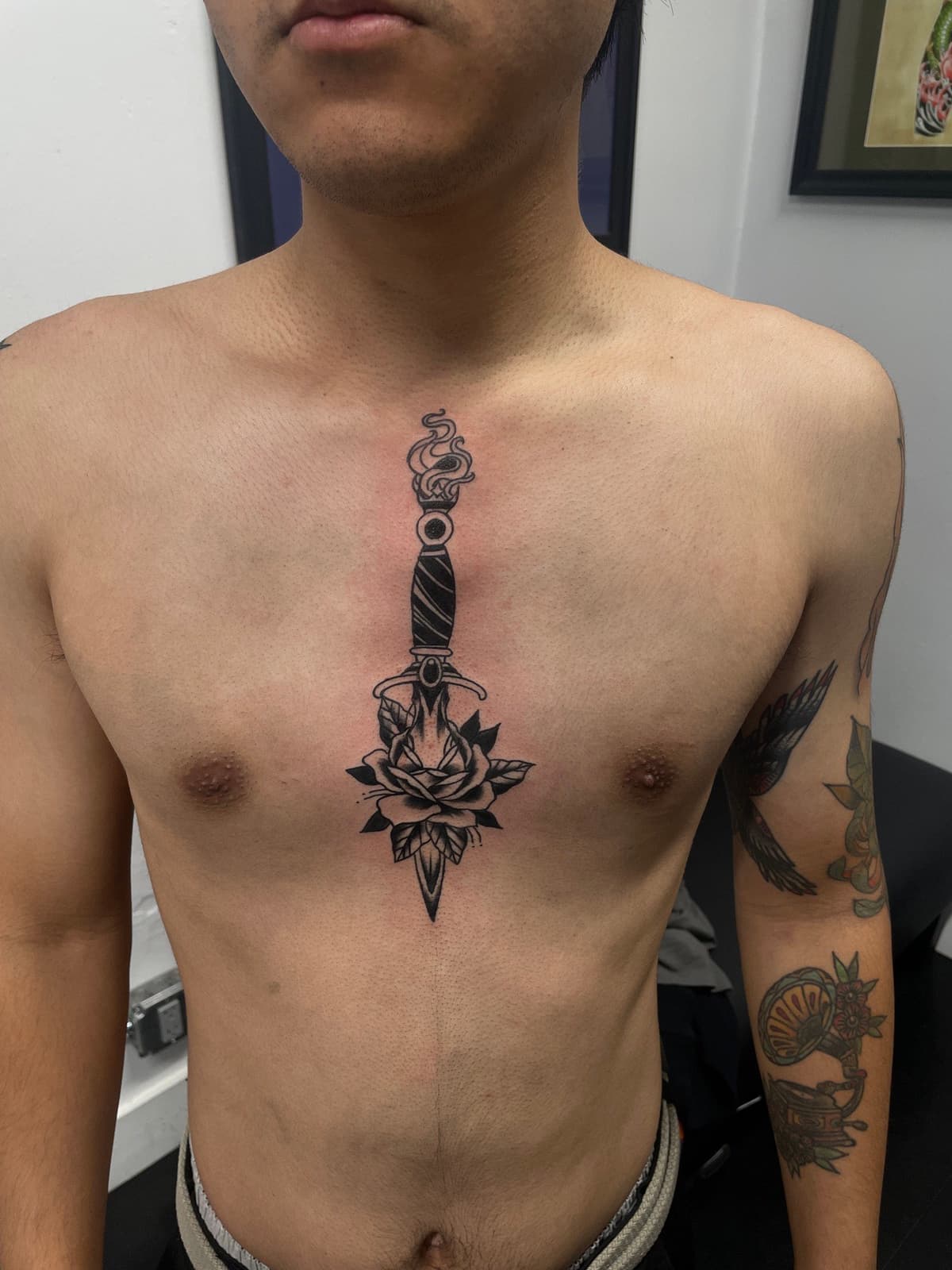 Blackwork tattoo dagger with snake and rose on sternum chest in Los Angeles