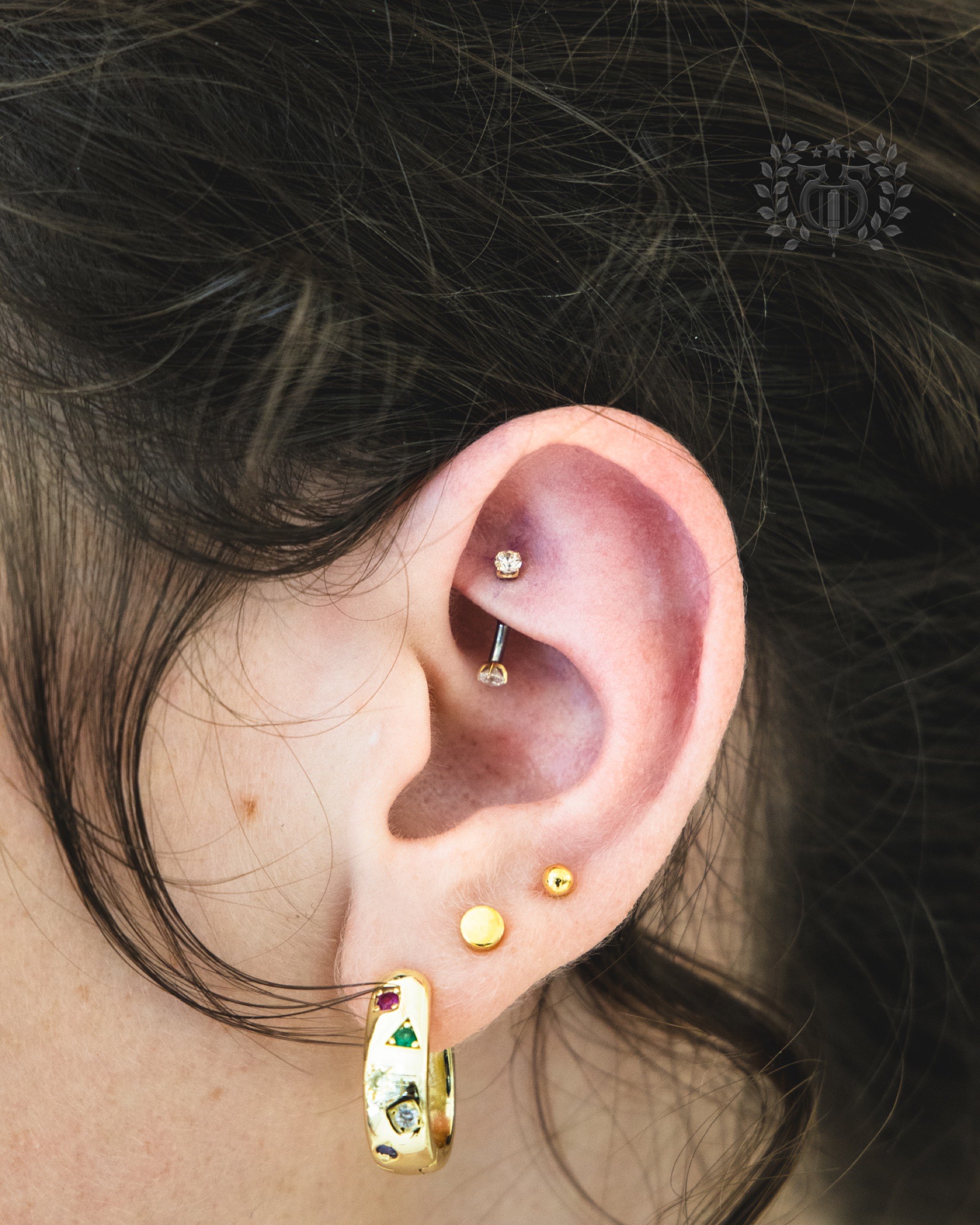 Close-up rook piercing with CZ curved barbell and gold gemstone lobe hoop at Apollo Studio Los Angeles