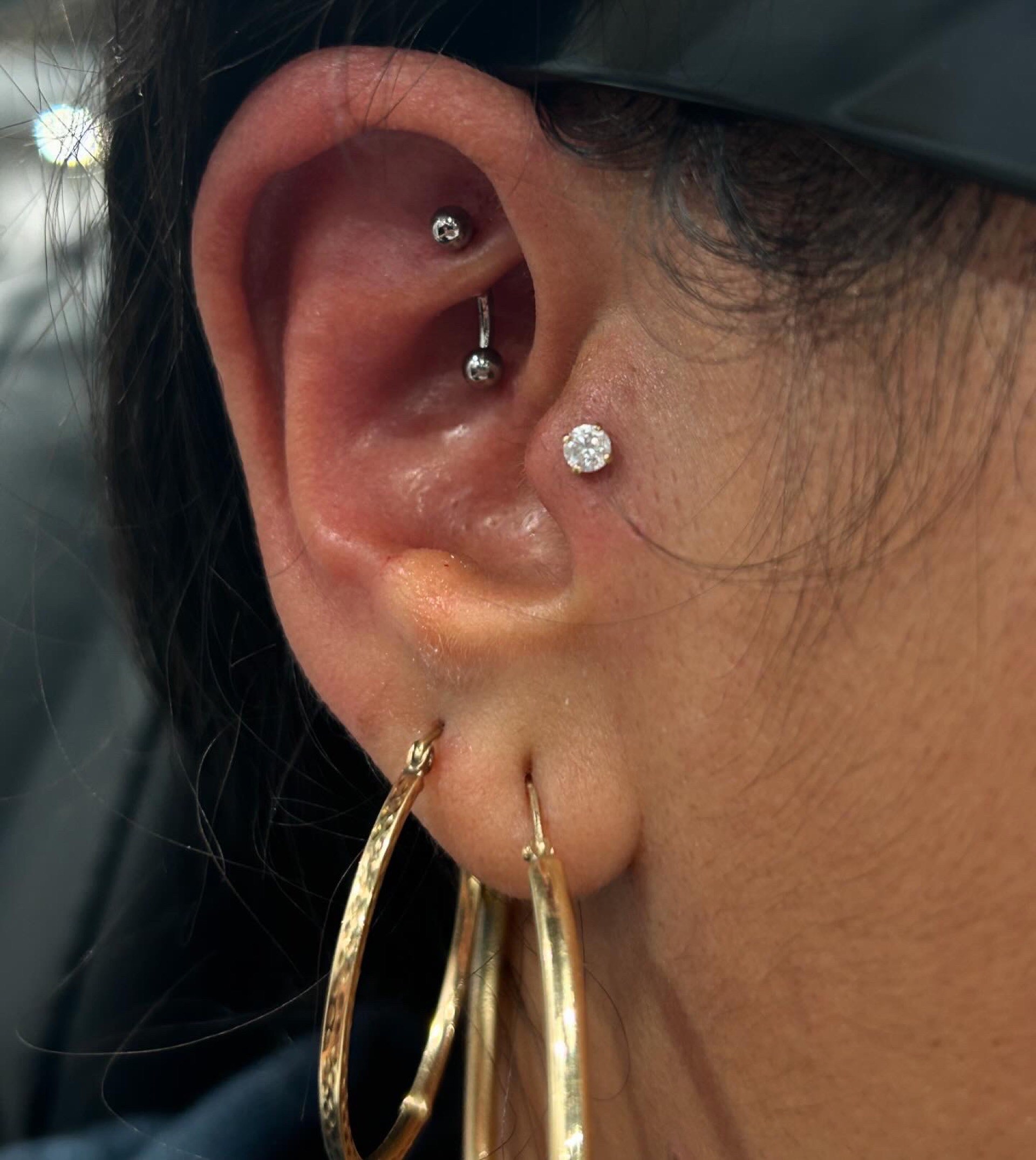 Rook piercing with curved barbell tragus CZ stud and large gold lobe hoops at Apollo Studio Los Angeles