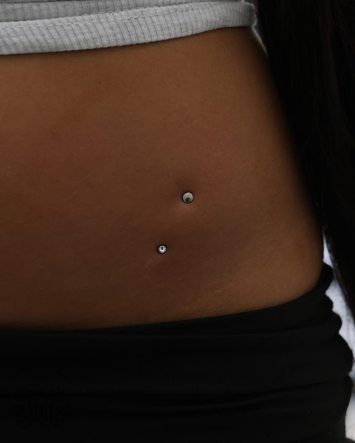Double surface anchor dermal piercings on lower abdomen with CZ tops at Apollo Studio