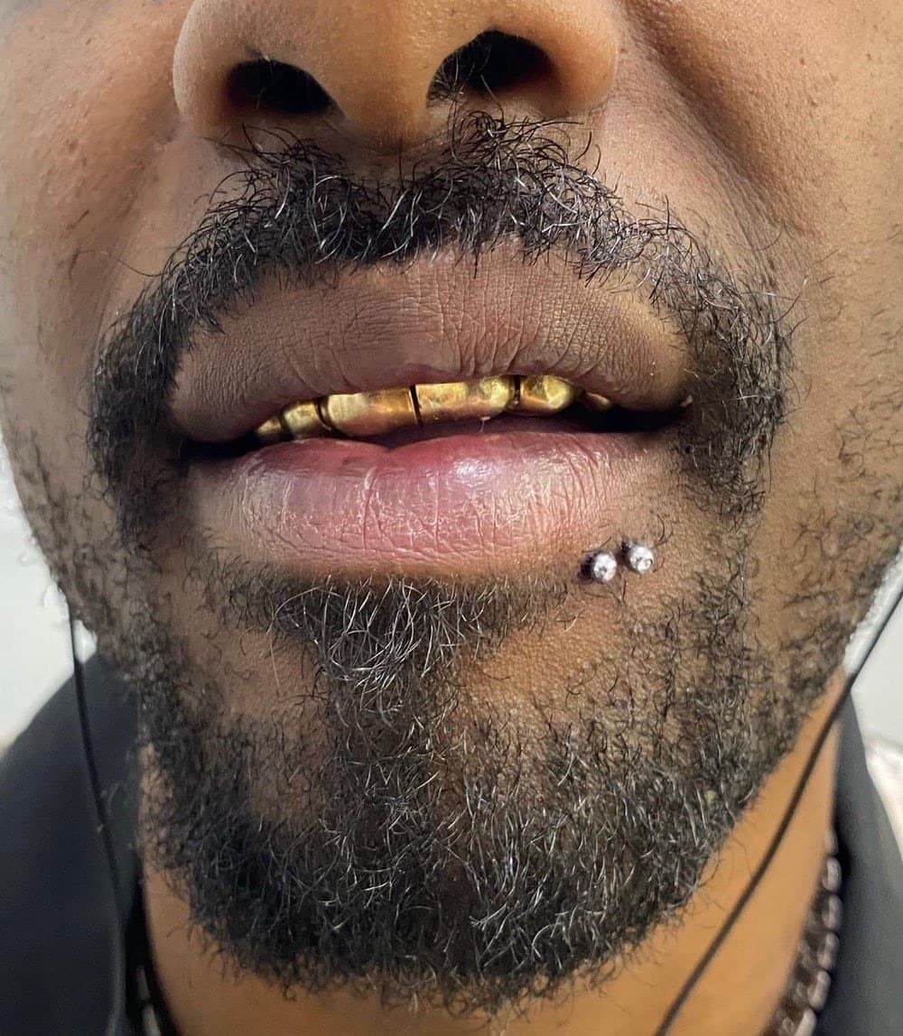 Labret piercing with double CZ studs on male client with gold grillz at Apollo Studio