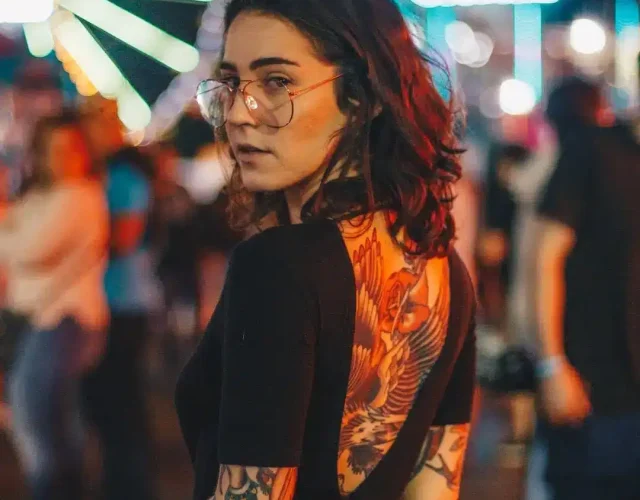 A woman with a large back tattoo cover up of a bird, set against a vibrant urban backdrop.